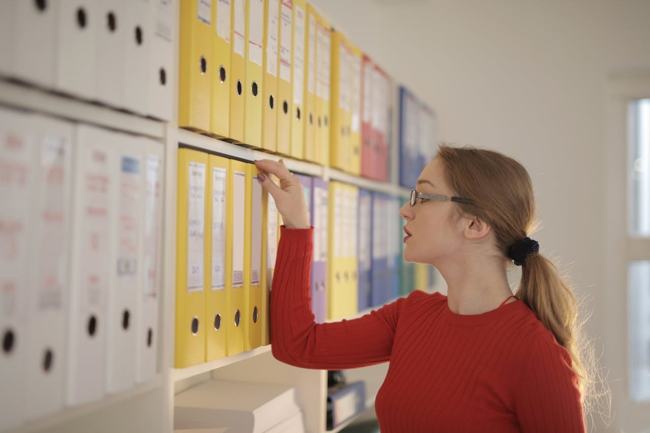 A focused woman in the office organizing and searching through colorful binders.